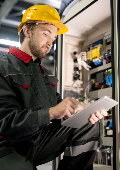 Young bearded engineer in workwear and hardhat using OEE software to review six big losses